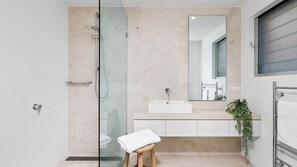 Une salle de bain moderne avec une douche à parois de verre, un lavabo blanc et un tabouret en bois.