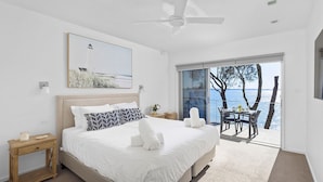 Une chambre moderne avec un grand lit, un ventilateur de plafond, un tableau et un balcon offrant une vue sur la mer.