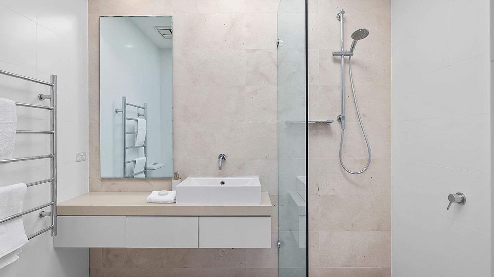 Une salle de bain moderne avec une douche à parois de verre, un lavabo blanc et un miroir au-dessus du lavabo.