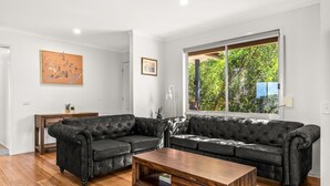 Ein Wohnzimmer mit einem Ecksofa, einem Holztisch und einem großen Fenster mit Blick auf Grünflächen.