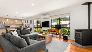 Una sala de estar moderna con un sofá gris, una mesa de centro y un televisor. Se ve una cocina al fondo con armarios y un microondas.