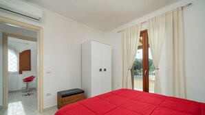 A bedroom with a red bedspread, a wardrobe, a wicker bench, and a red chair.