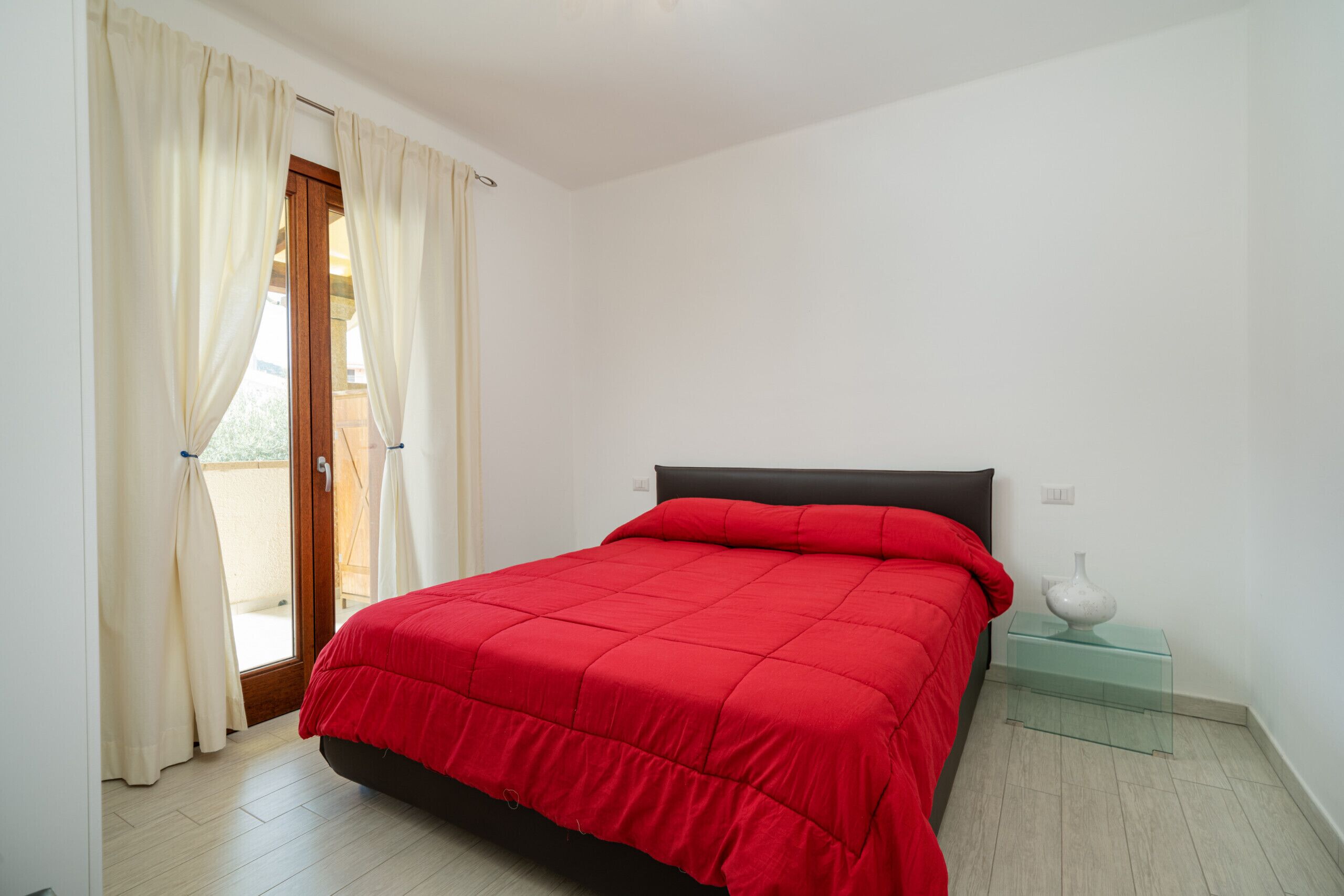 A bedroom with a bed, curtains, a nightstand, and a vase.