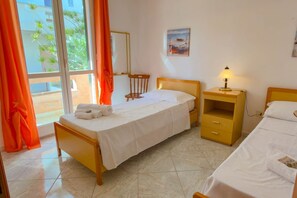 A hotel room with a bed, a nightstand, a chair, a window with curtains, and a painting on the wall.