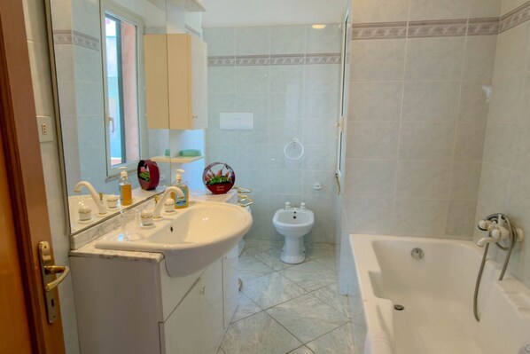 A bathroom with a sink, mirror, bidet, and bathtub.