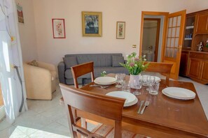 A dining area with a wooden table set for four, a grey sofa, and a cabinet with glass doors in the background.