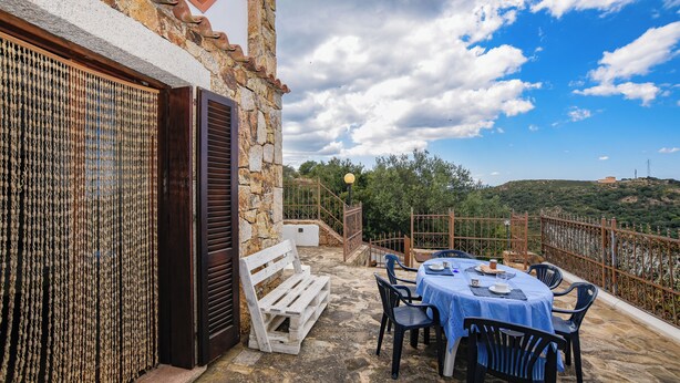 A stone building with a balcony, a table with chairs, and a view of the landscape.