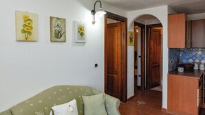 A living room with a sofa, a kitchen with wooden cabinets, and wall-mounted artwork.