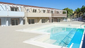A swimming pool with a tiled deck, a building with multiple windows, and a clear blue sky. - Affittimoderni Viddalba Sea Stars - VISM11 (Viddalba)