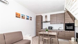 A modern kitchen with wooden cabinets, a dining area with a table and chairs, and a sofa in a living area. - Affittimoderni Viddalba Sea Stars - VISM11 (Viddalba)