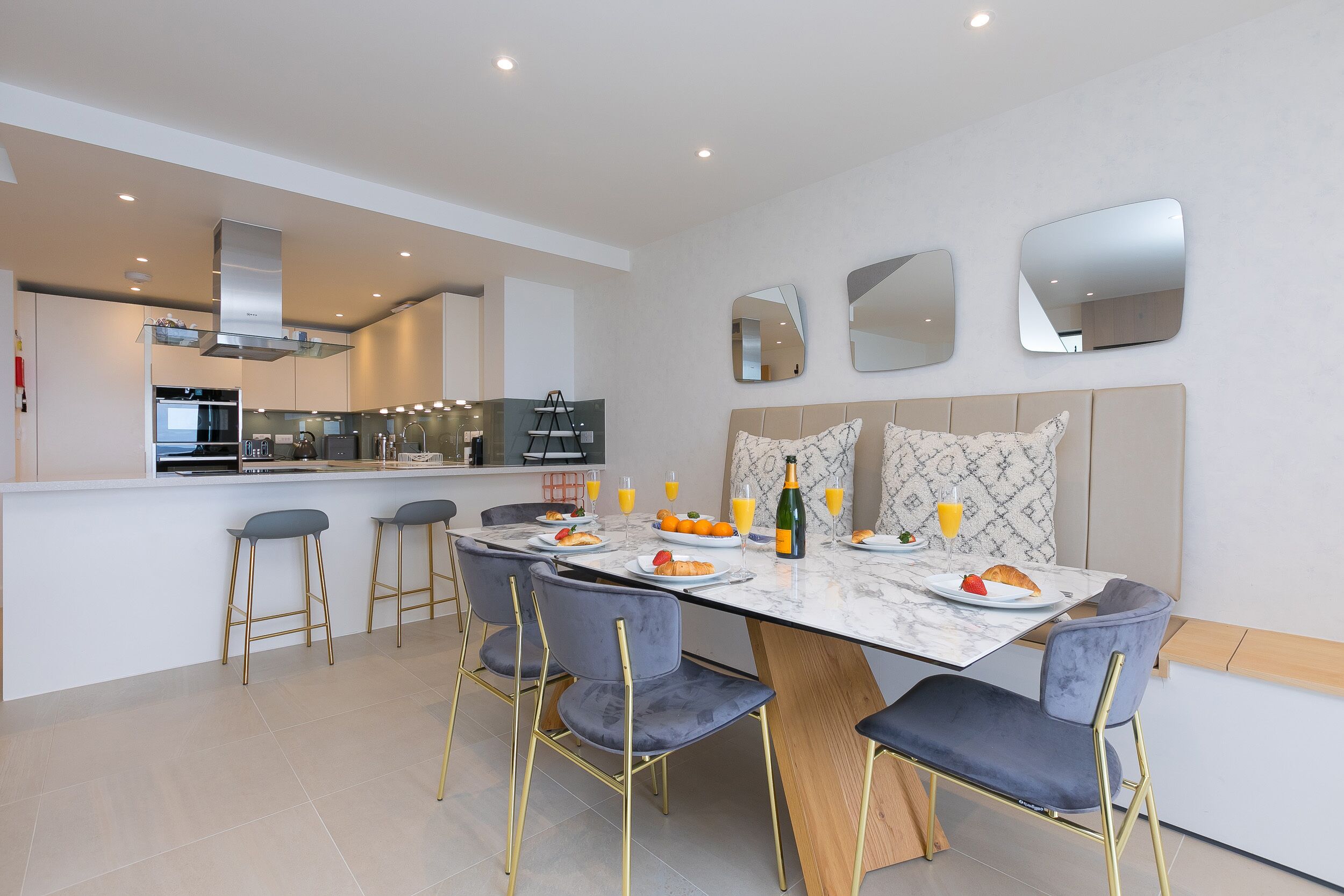 A modern kitchen with a central island, bar stools, and a dining table set for breakfast.