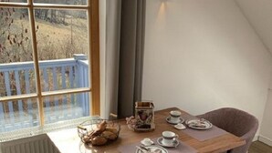 Un'area pranzo con un tavolo apparecchiato per due, una finestra che si affaccia su una foresta e un termosifone sotto la finestra.