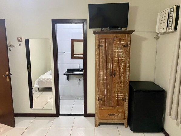 Una habitación con un armario de madera, un mueble negro, un televisor montado en la pared y un espejo en la puerta.