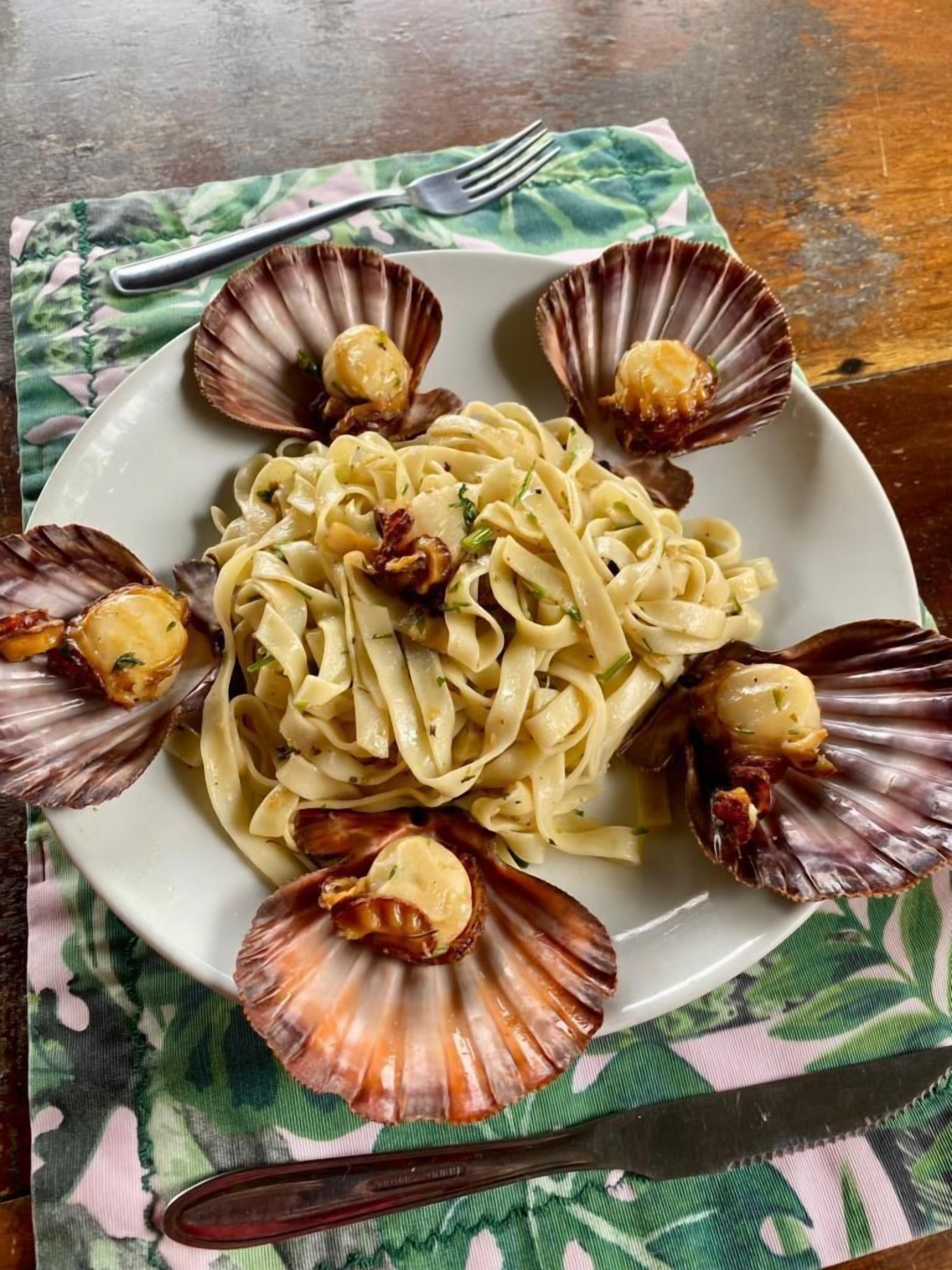 A plate of pasta with scallops on a table with a green and white cloth.