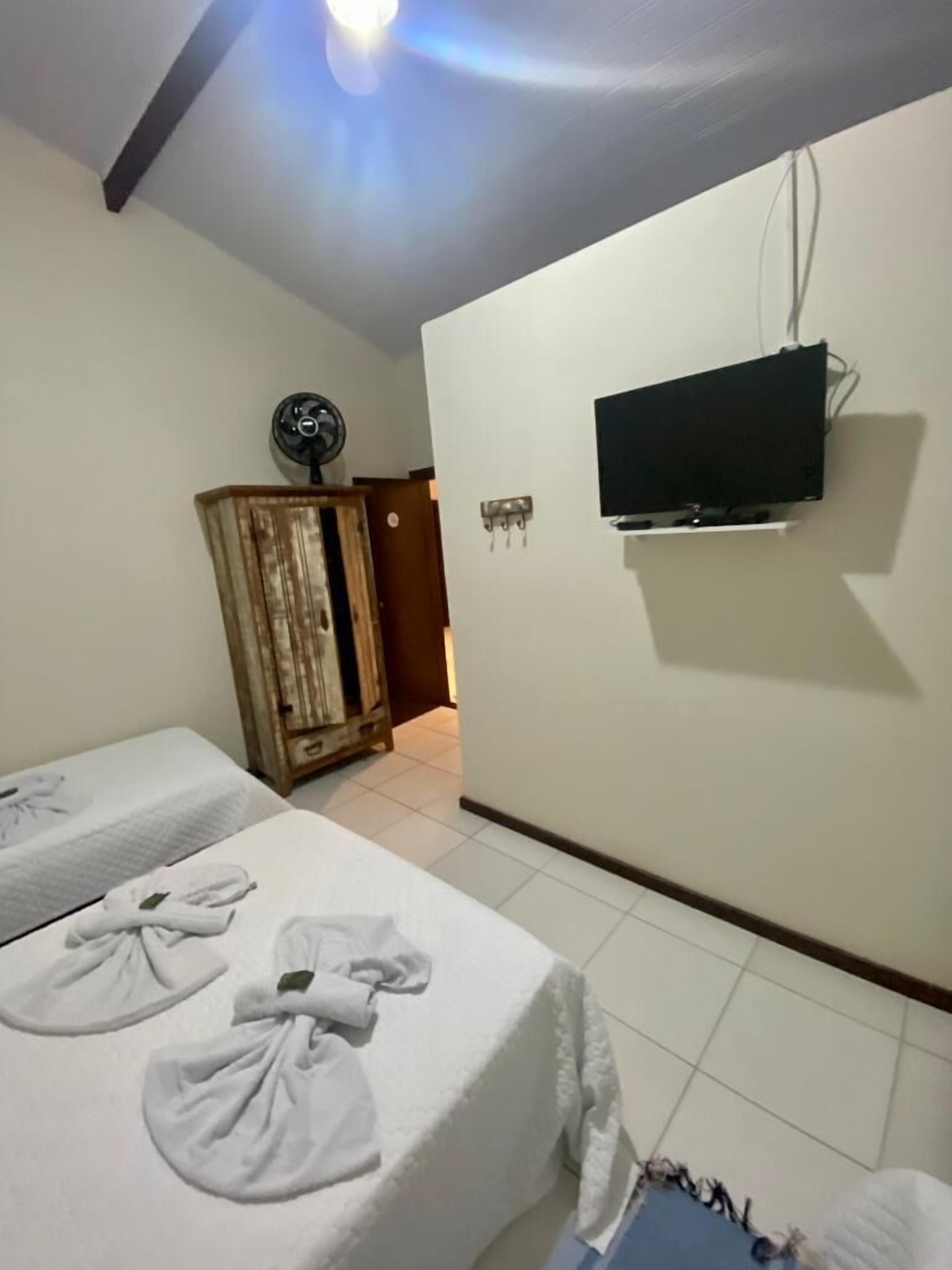 A hotel room with two beds, a television mounted on the wall, a wooden cabinet, and a fan on the ceiling.
