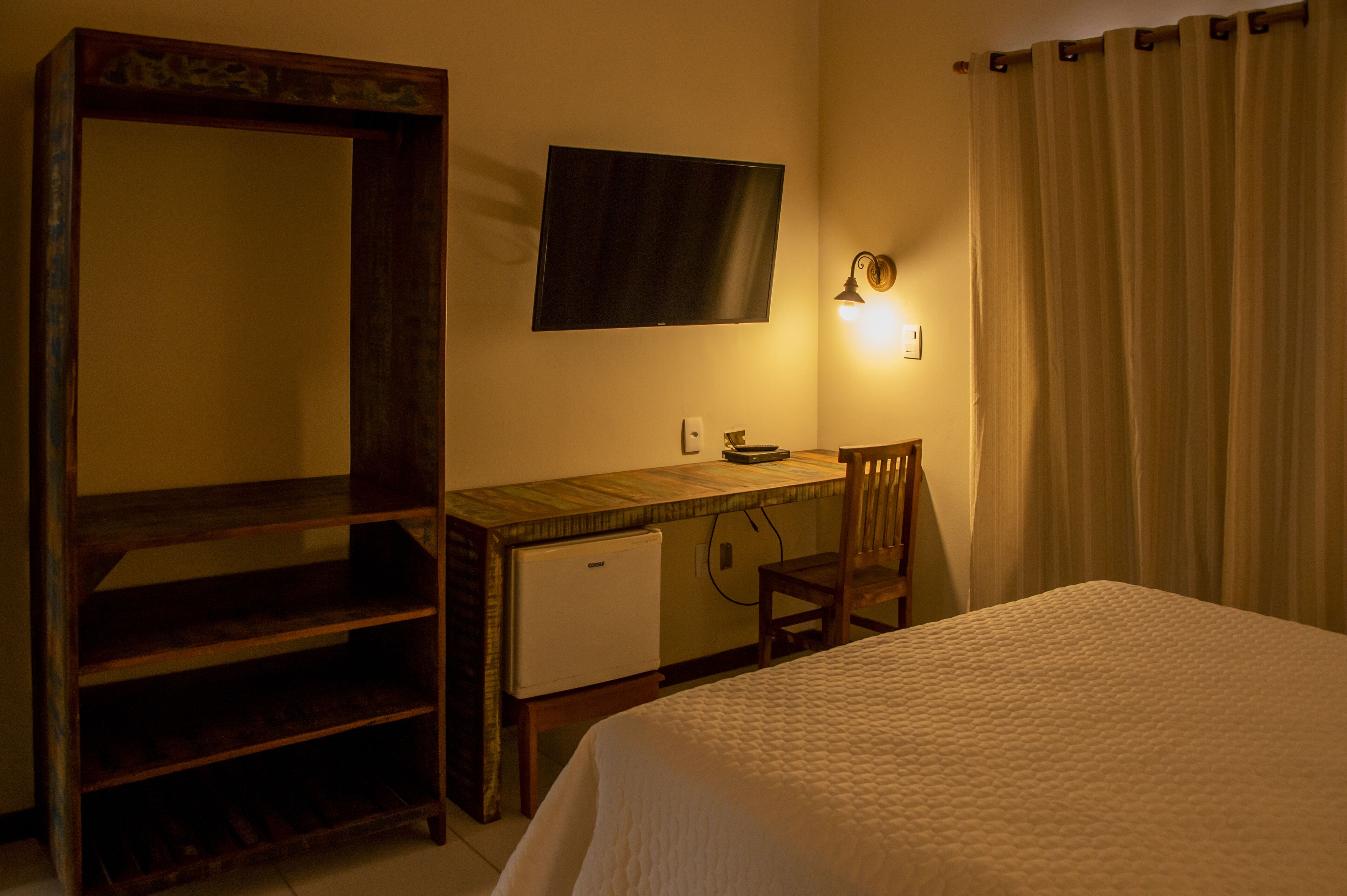 Une chambre comprenant un lit, un bureau, une chaise, un téléviseur et un petit réfrigérateur.