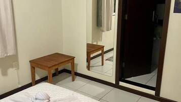 A hotel room with a bed, a small wooden table, a mirror, a TV mounted on the wall, and a bathroom door.