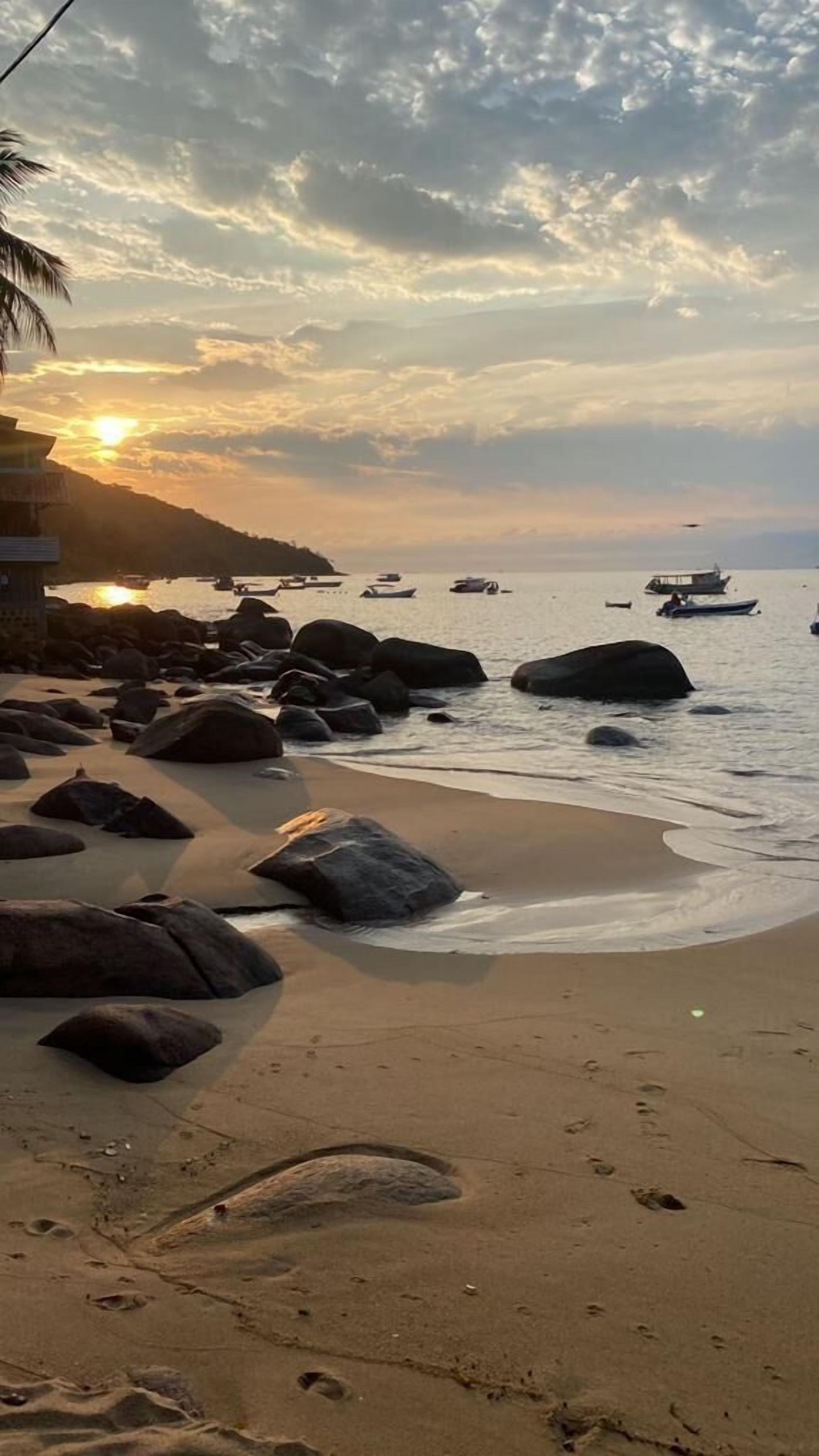 Una playa con grandes rocas, una orilla arenosa y barcos en el agua.