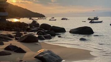 Una playa con grandes rocas, una orilla arenosa y barcos en el agua.