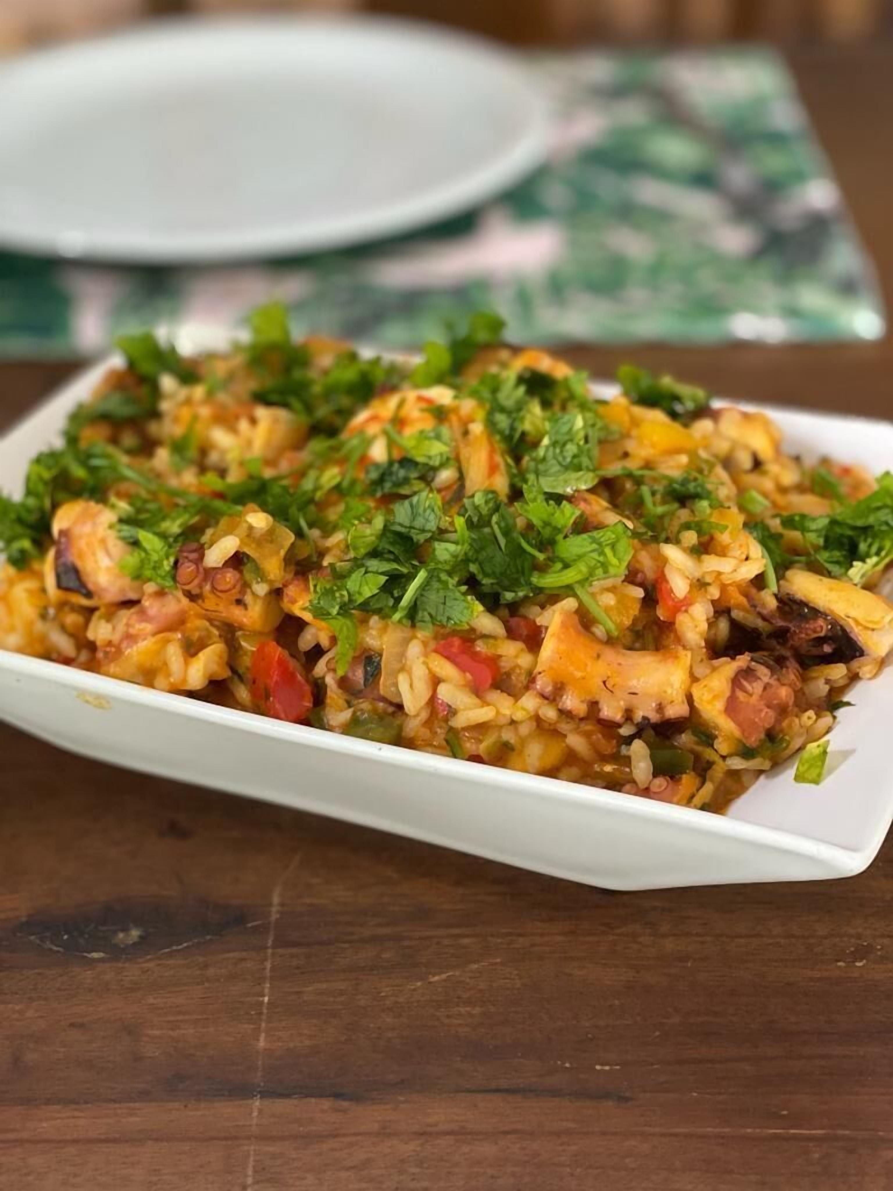 Un plato de arroz con verduras y carne, adornado con hierbas, servido en un plato blanco.