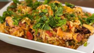 Un plato de arroz con verduras y carne, adornado con hierbas, servido en un plato blanco.