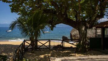 A beach with a wooden fence, a large tree, and a view of the ocean.