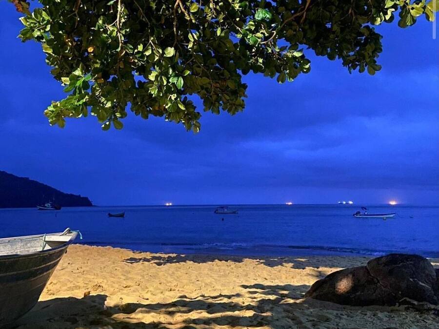 Una playa con barcos, cielo despejado y mar tranquilo.