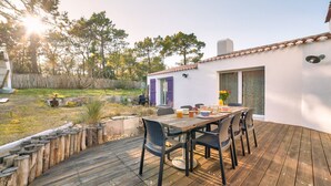 A wooden deck with a table and chairs, surrounded by a white building with purple shutters and a window with a lattice screen. - Private access to the beach - House for 6 (Barbâtre)