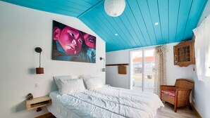 A bedroom with a large bed, a painting, a wicker chair, and a view of the outside. - Private access to the beach - House for 6 (Barbâtre)