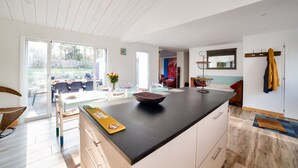 A modern kitchen with a large island, sliding glass doors leading to a patio, and a dining area visible through the doors. - Private access to the beach - House for 6 (Barbâtre)
