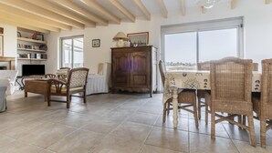 A spacious living room with a high ceiling, wooden beams, a large window, wicker furniture, and a television. - Nice house and its veranda for a nice holiday (Saint-Philibert)