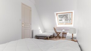 A bedroom with a large bed, a window with a view of trees, a chair, a small table, and a lamp. - Nice house and its veranda for a nice holiday (Saint-Philibert)