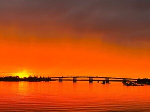 Un sol de ponent sobre un cos d'aigua tranquil·la, amb un pont al fons.