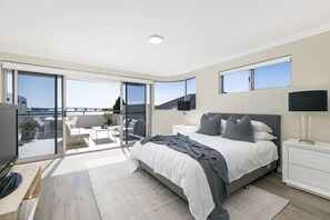 Ein modernes Schlafzimmer mit einem großen Bett, einem Fernseher, einem Nachttisch, einer Lampe und einem Balkon mit Blick.