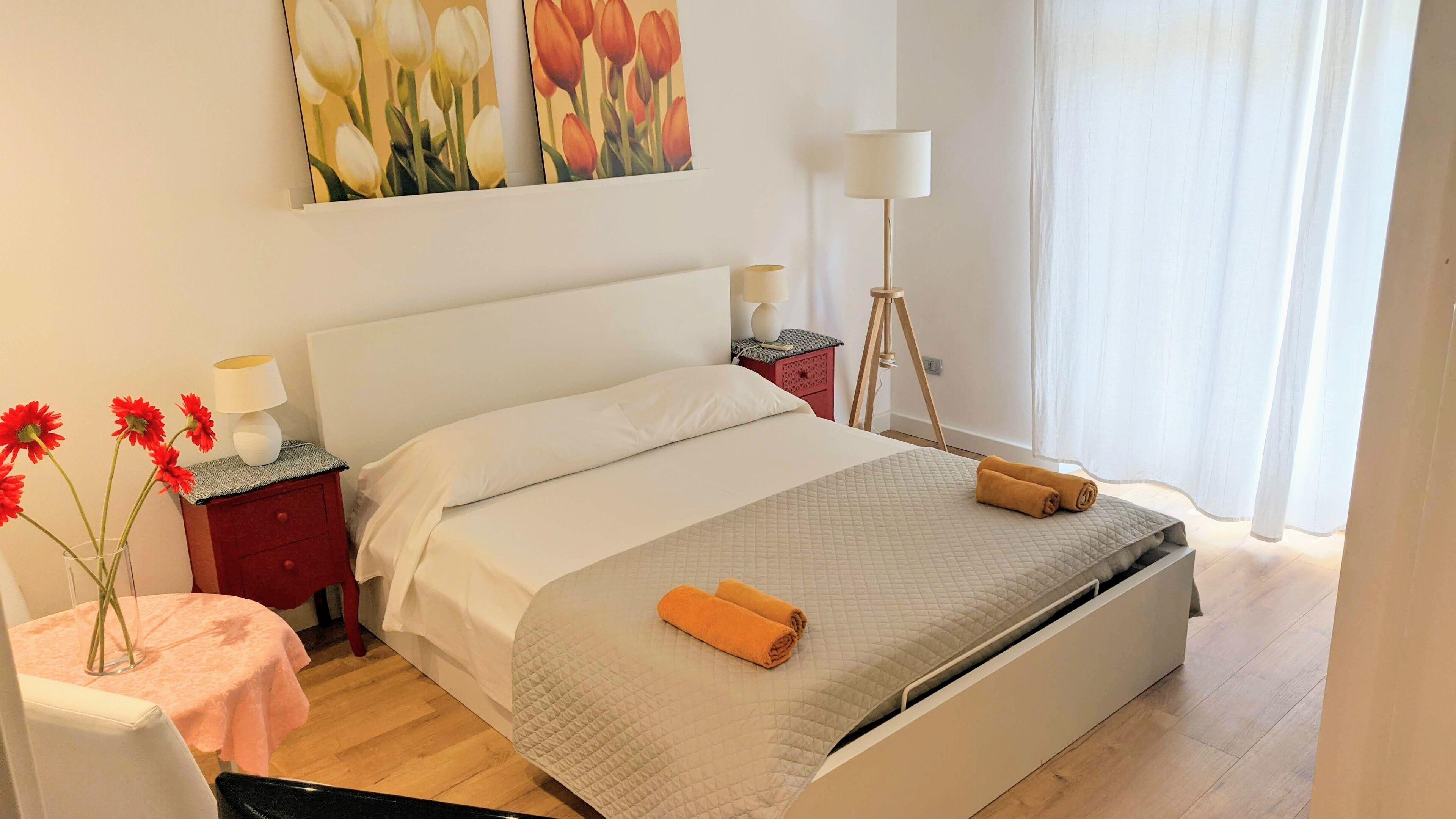 A neatly arranged bedroom with a bed, bedside tables, a lamp, and a vase with flowers.