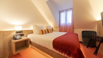 A hotel room with a bed, a nightstand with a phone, a chair, and a window with curtains.