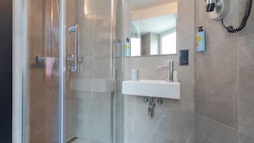 Un baño moderno con ducha de vidrio, lavamanos blanco y espejo.