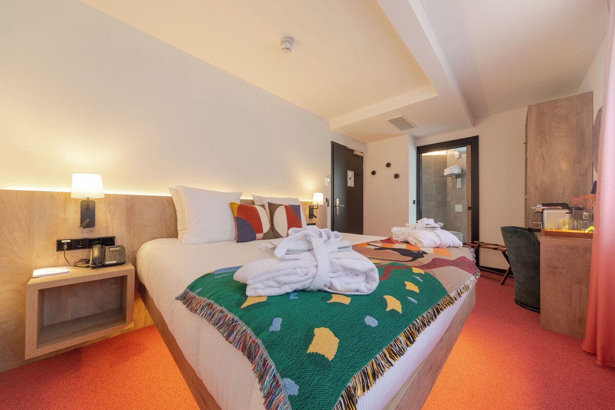 A hotel room with a bed, a desk, a chair, a lamp, and a telephone.