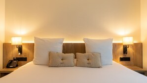 A neatly made bed with two white pillows and two smaller decorative pillows, flanked by two bedside tables with lamps and a phone. - Kazakiwi (Luxembourg City)