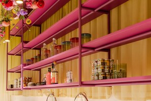 Une étagère métallique rose contenant divers pots et bouteilles, qui renferment probablement des condiments ou des ustensiles de cuisine.