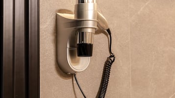 A wall-mounted hair dryer with a coiled cord, attached to a wall with a textured surface.