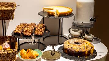Una mesa de buffet con diversos postres, incluyendo un pastel de queso, un pastel ring y varios tipos de pan.