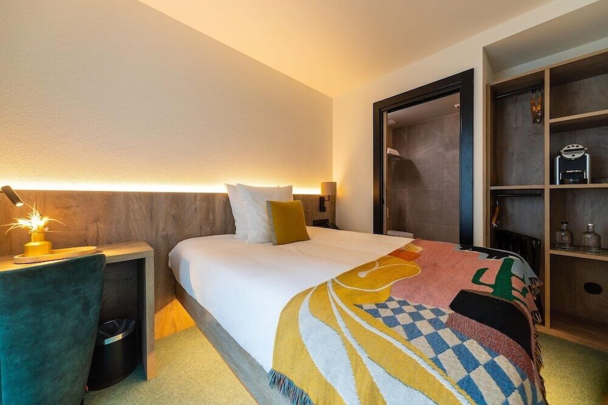 A hotel room with a bed, bedside table, lamp, and a wardrobe.