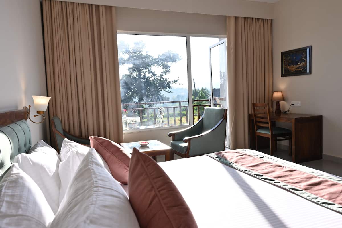 Habitación de hotel con cama, escritorio, silla, ventana con cortinas y vistas al exterior.