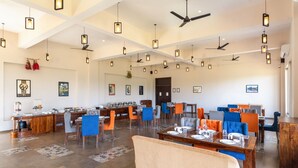 A spacious dining area with multiple tables and chairs, ceiling fans, and hanging pendant lights. - Kumbhal Exotica Resort Kumbhalgarh (Kumbhalgarh)