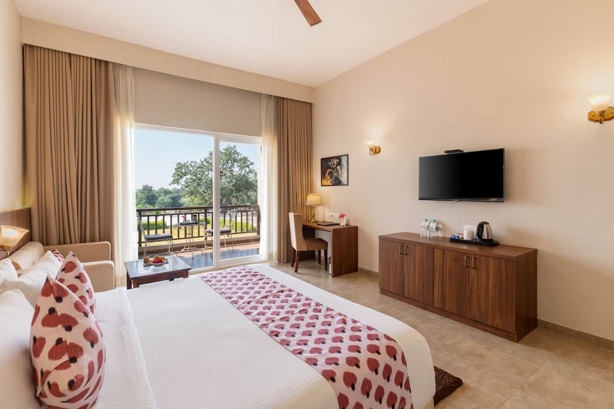 Habitación de hotel con cama, escritorio, televisor, balcón con vistas y zona de comedor.
