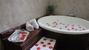 A bathroom with a bathtub, a glass of water, a towel, and a tray with rose petals. - PARADIES HOTEL EXPRESS (Jarinu)