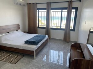 A bedroom with a bed, a desk, and a view of the beach through large windows.