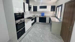 A modern kitchen with white and black cabinetry, a built-in oven, and a marble floor. - SEA VIEW APARTMENT (DAKAR)