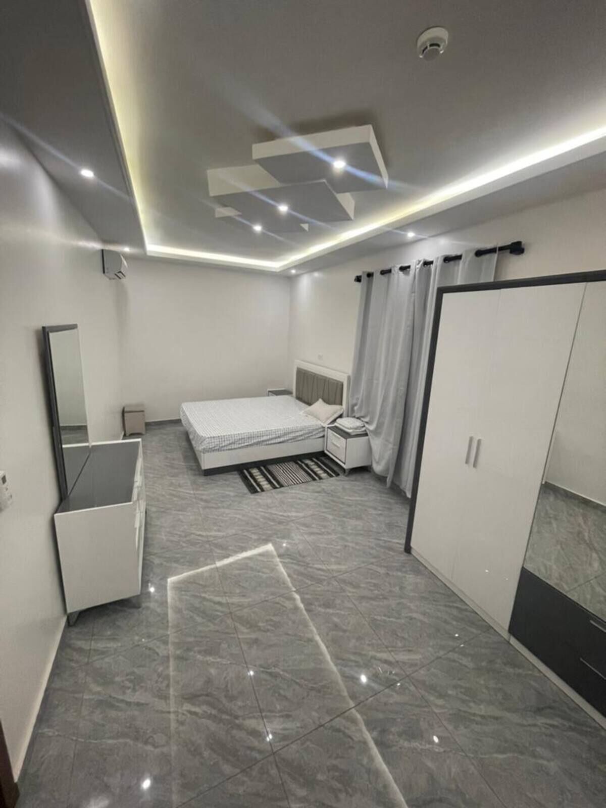 A modern bedroom with a bed, bedside table, wardrobe, and a mirror.